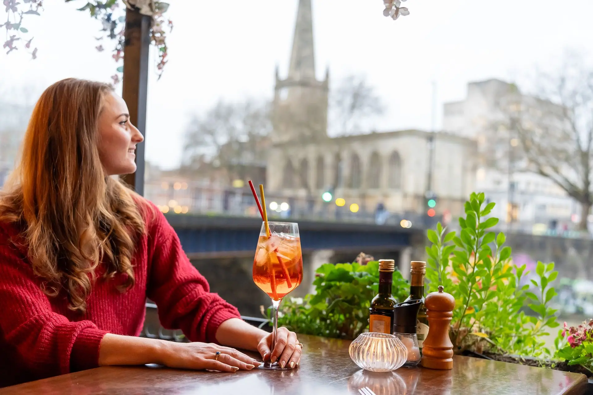 Guest with an Aperol spritz on Bella Vista's riverside terrace, a church spire behind, Bristol