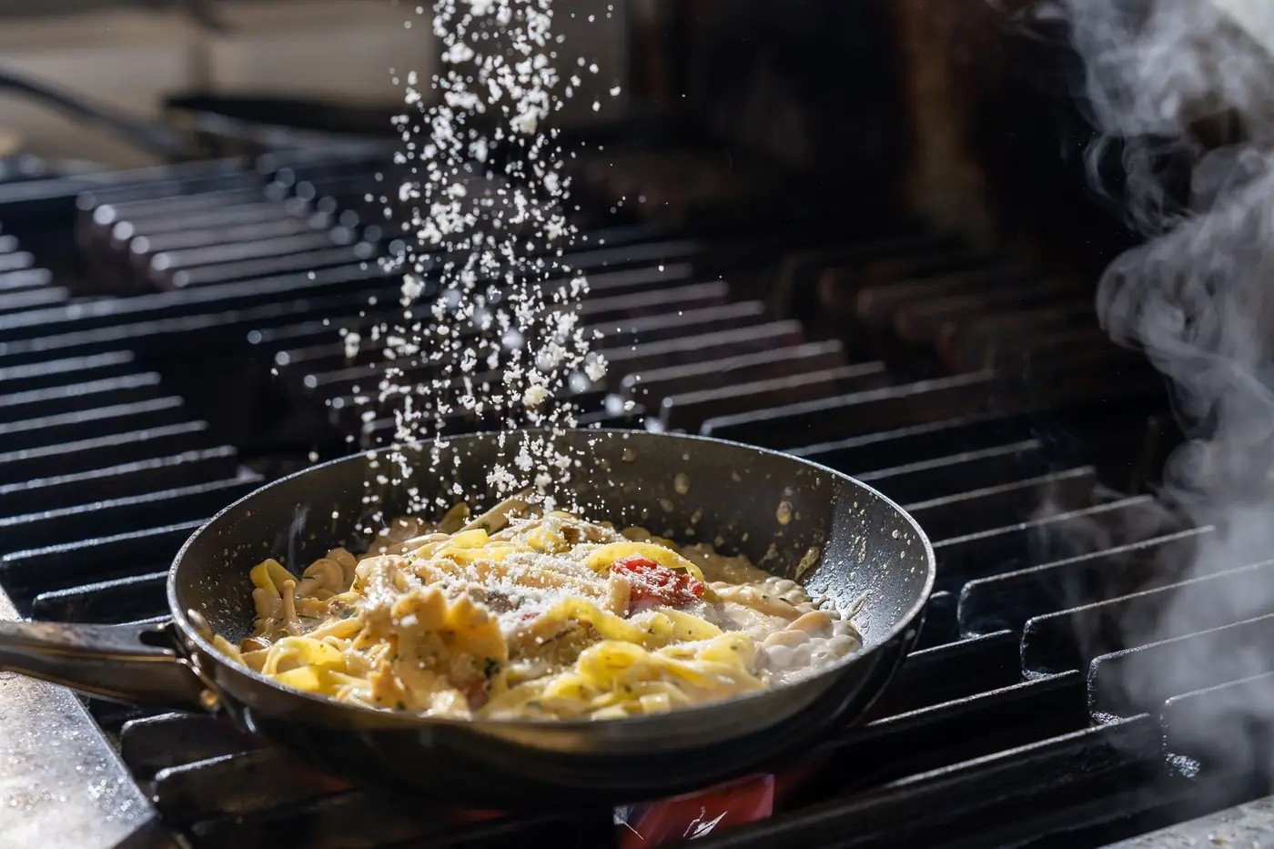 Parmesan falling onto pasta in a hot pan in Bella Vista's kitchen, Bristol