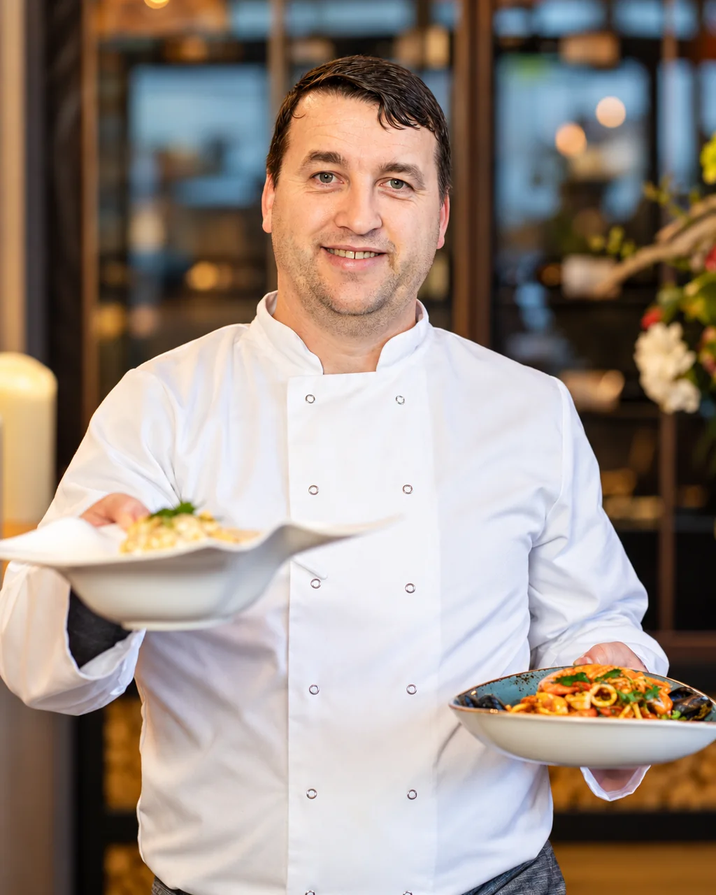 Petrit, owner of Bella Vista Bristol, in chef's whites holding two plates of pasta