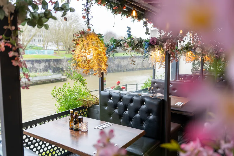 Riverside terrace booth beneath flower-covered lanterns at Bella Vista, Bristol